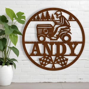Pode incluir: Placa de madeira marrom com uma silhueta de uma pessoa dirigindo um cortador de grama, árvores e a palavra "ANDY" em uma fonte grande. A placa também tem um design de bandeira quadriculada.