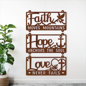 Puede incluir: Tres piezas de arte mural de metal marrón con citas inspiradoras: "Faith Moves Mountains", "Hope Anchors the Soul" y "Love Never Fails". Cada pieza presenta elementos decorativos como montañas, una paloma, un ancla, una cruz y corazones.