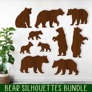 May include: A set of ten brown bear silhouette cutouts in various sizes. The bears are arranged on a white wall with a green plant in a woven basket in the lower left corner. The text "BEAR SILHOUETTES BUNDLE" is at the bottom of the image.