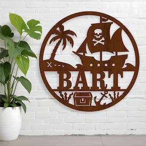 May include: A round, brown metal pirate-themed wall art piece. The design includes a pirate ship with a skull and crossbones, a palm tree, the name "BART", a treasure chest, and an anchor. The art is mounted on a white brick wall.