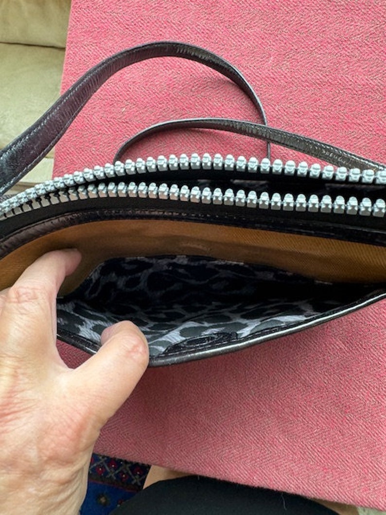 Puede incluir: Un bolso de hombro de cuero negro con cierre de cremallera y forro de estampado de leopardo. El bolso tiene una sola correa.