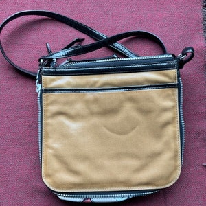 Puede incluir: Un bolso bandolera de cuero marr&oacute;n con una solapa de cuero negro y una cremallera negra. El bolso tiene una correa larga negra.