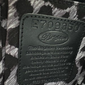 Puede incluir: Etiqueta de cuero negro con costuras blancas y el texto "E709350 Brighton The Brighton Collection handbags are individually crafted in China from quality leathers. Any marks on the surface are made by the leather itself and should not be seen as a defect. Made in China."