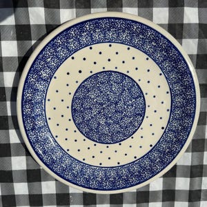 May include: A blue and white ceramic plate with a polka dot pattern. The plate has a raised rim and a textured surface.