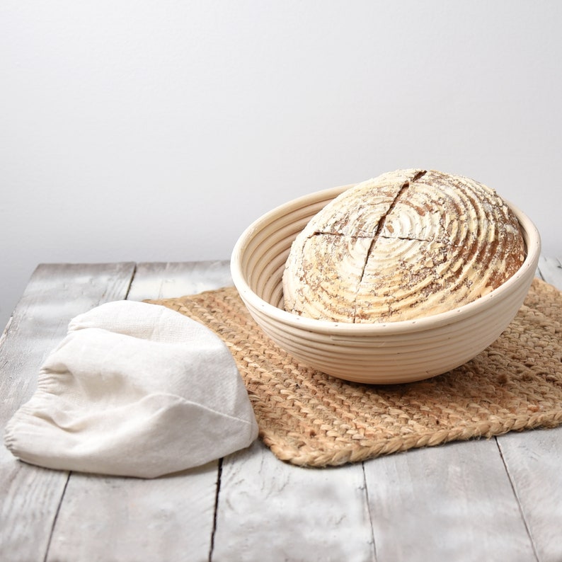 proofing basket liner folded outside on a grey table with banneton basket on a mat with sourdough bread inside