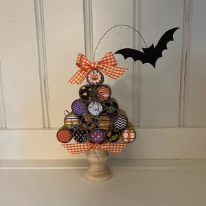May include: A Halloween-themed cork tree with a black bat decoration. The tree is decorated with orange, purple and black patterned corks and a white and orange checked ribbon.