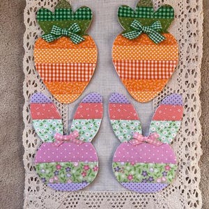 May include: Four fabric Easter-themed coasters. Two are carrot shaped with orange and green checkered patterns. Two are bunny shaped with pink, green, and purple floral patterns.