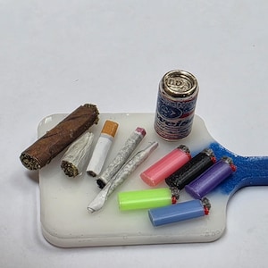 May include: A miniature set featuring a brown cigar, two rolled cigarettes, one standard cigarette, a small beverage can labeled Budweiser, and five colorful plastic lighters in pink, black, purple, lime green, and light blue on a white serving board.