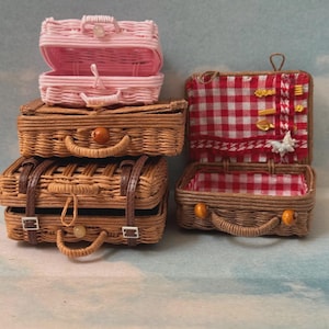 May include: Miniature woven picnic baskets in shades of pink and brown. One basket is open, revealing a red and white checkered interior. Other baskets are closed, with handles and clasps.