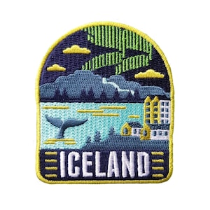 May include: An embroidered patch featuring a blue and green landscape, a whale tail, and a small town. The patch is yellow with the word "ICELAND" in white.