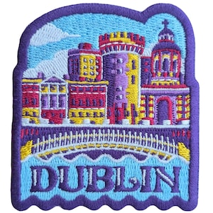 May include: Embroidered patch depicting Dublin, Ireland. The design shows buildings, a bridge, and the city name in blue. The patch has a purple border and a light blue sky. A souvenir item.