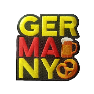 May include: A black embroidered patch with the words "GERMAN" in yellow, "MA" in red, and "NY" in yellow. A cartoon image of a beer stein and a pretzel are in the center of the patch.