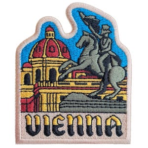 Könnte beinhalten: Ein gestickter Aufnäher mit einer farbenfrohen Darstellung eines Gebäudes mit einer Kuppel und einer Statue einer Person zu Pferd. Der Text "VIENNA" ist in schwarzen Buchstaben auf beigefarbenem Hintergrund gestickt.