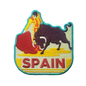 May include: Embroidered patch featuring a matador in a yellow and orange suit with a red cape, facing a dark purple bull. The word "SPAIN" is embroidered in red letters on a yellow background, outlined in teal.