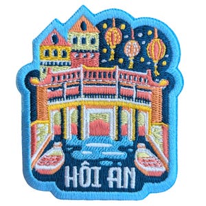 Könnte beinhalten: Gestickter Aufnäher mit einer farbenfrohen Illustration einer Brücke und Gebäuden mit Laternen. Der Text "HÓI AN" befindet sich unter dem Bild.