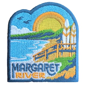 Op de afbeelding: Geborduurde patch met een blauwe, groene en gele zonsondergangscène boven een strand met een houten promenade en twee surfplanken. De tekst "Margaret River" is onderaan in wit geborduurd.