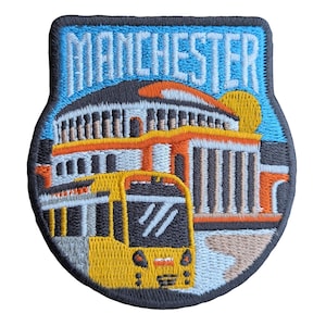May include: An embroidered patch featuring the word "Manchester" in white lettering on a blue and white background. The patch depicts a yellow tram in front of a building with orange and white details.