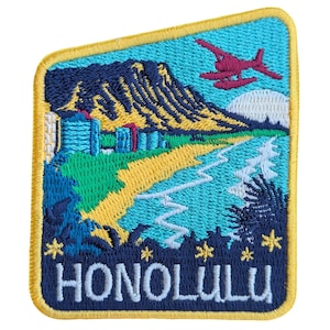 May include: An embroidered patch with a yellow border and a blue background. The patch depicts a scene of a beach with a mountain in the background, a red airplane flying overhead, and the text "HONOLULU" in white lettering.