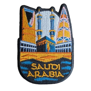 Puede incluir: Parche bordado con una representación colorida de la Kaaba en La Meca, Arabia Saudita. El parche es negro con detalles en azul, amarillo y blanco. El texto "SAUDI ARABIA" está bordado en amarillo sobre un fondo azul.