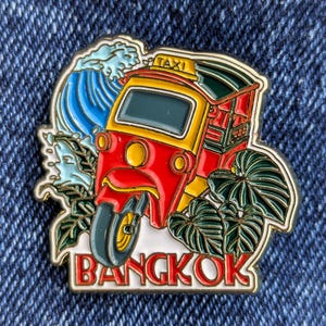 May include: A red and yellow tuk-tuk with a "TAXI" sign on the roof, surrounded by green leaves and a blue wave. The words "BANGKOK" are written in white on a gold background.