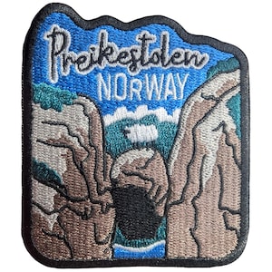 May include: Embroidered patch featuring the text "Preikestolen NORWAY" above a scenic landscape. The patch depicts a blue sky, brown cliffs, and a green and blue body of water. The patch has a black border.