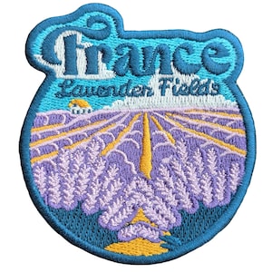 May include: Embroidered patch with a blue background and the text "France Lavender Fields". The patch features a stylized image of a lavender field with a yellow path leading to a small house in the distance.