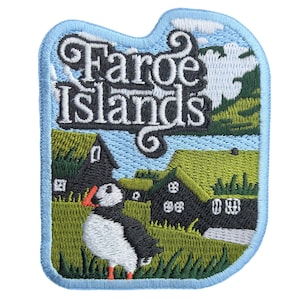 May include: Embroidered patch featuring the text "Faroe Islands" above a scenic landscape. The design includes a puffin, traditional houses with green roofs, and a blue sky with clouds. The patch has a light blue border.