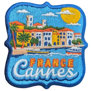 Op de afbeelding: Geborduurde patch met een kustlandschap met gebouwen, palmbomen en boten onder een gele zon. De tekst "FRANCE CANNES" is geborduurd in wit en oranje op een blauwe achtergrond.
