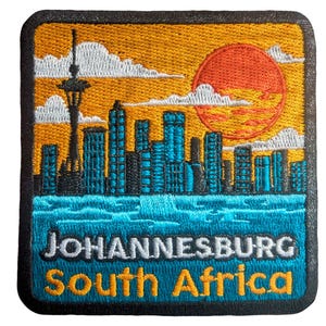 Könnte beinhalten: Gestickter Aufnäher mit einer Stadtlandschaft mit Sonnenuntergang, Wolken und einem Turm. Der Aufnäher trägt den Text "JOHANNESBURG South Africa" in Weiß und Gelb. Das Design umfasst eine Skyline mit türkisfarbenen Gebäuden und einer roten Sonne.