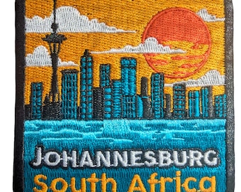 Op de afbeelding: Geborduurde patch met een stadsgezicht met een zonsondergang, wolken en een toren. De patch heeft de tekst "JOHANNESBURG South Africa" in wit en geel. Het ontwerp bevat een skyline met turquoise gebouwen en een rode zon.