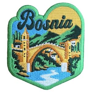 Pode incluir: Etiqueta bordada com contorno verde em forma de coração. A etiqueta apresenta uma ponte amarela com um rio azul e árvores verdes. O texto "Bosnia" é bordado em letras amarelas e pretas.