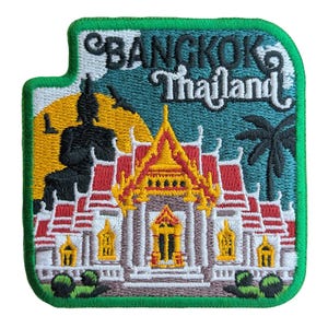 以下が含まれることがあります： 緑色の縁取りのある刺繍パッチで、タイのバンコクにある寺院が描かれています。寺院は薄いグレーで、赤と黄色のアクセントが付けられています。"バンコク タイランド"という文字が、青い背景に白で刺繍されています。