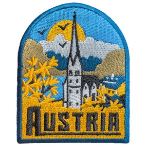 May include: Embroidered patch depicting an Austrian scene with a church, mountains, and a lake under a blue sky and yellow sun. The word "AUSTRIA" is embroidered in yellow and black.