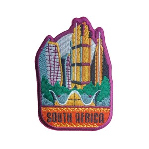 May include: Embroidered patch featuring a colourful cityscape and the text "South Africa" in a gold and orange banner. The patch is pink and has a white background.
