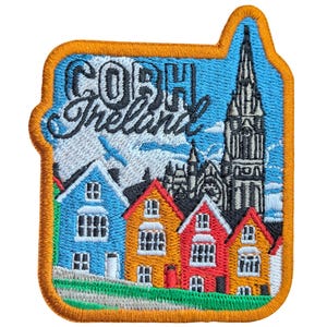 May include: Embroidered patch featuring a colorful depiction of Cobh, Ireland. The design includes the text "COBH Ireland" above a row of vibrant houses and a tall church spire against a blue sky. The patch has an orange border.