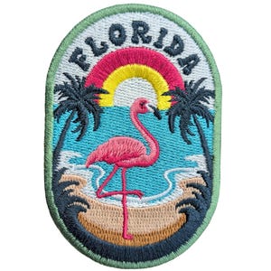 May include: Embroidered patch with a pink flamingo, palm trees, and a rainbow over a beach scene. The word "FLORIDA" is arched across the top in white letters. The patch has a green border.