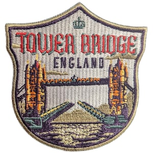 May include: Embroidered patch featuring Tower Bridge in London, England. The patch is shield-shaped with a cream background and a detailed image of the bridge in shades of orange, yellow, green, and purple. The text "TOWER BRIDGE ENGLAND" is embroidered in red.
