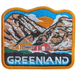 May include: Embroidered patch featuring a scenic Greenland landscape. The design includes two small houses, one orange and one red, set against a backdrop of mountains, a setting sun, and the word "GREENLAND" in white letters.