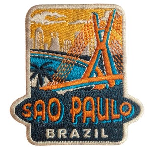 以下が含まれることがあります： サンパウロのスカイラインとオレンジと青のアクセントが施された橋が描かれた刺繍パッチ。「SAO PAULO BRAZIL」の文字がオレンジと白で、濃い青色の背景に、ベージュの縁取りが施されています。