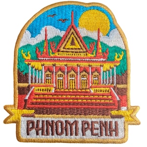 May include: Embroidered patch featuring a colorful depiction of a temple in Phnom Penh, Cambodia. The design includes a yellow sun, blue sky, and the text "PHNOM PENH" in white. The patch has a gold border and is likely for clothing or bags.
