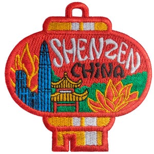 Op de afbeelding: Geborduurde patch in de vorm van een rode lantaarn, met de tekst "SHENZEN CHINA" in het wit. De patch bevat afbeeldingen van een stadsgezicht, een pagode en een lotusbloem, allemaal in levendige kleuren.