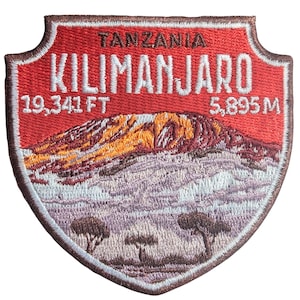 Puede incluir: Parche bordado con el monte Kilimanjaro en Tanzania. El parche rojo tiene texto blanco que dice "TANZANIA KILIMANJARO" y la elevación en pies y metros. La montaña está representada en tonos naranja, marrón y morado.
