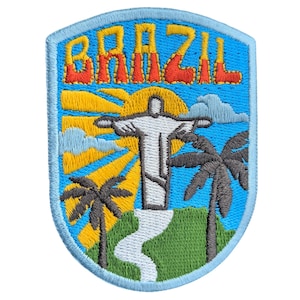 Op de afbeelding: Geborduurde patch met het woord "BRAZIL" in oranje letters. Het ontwerp omvat het Christusbeeld, palmbomen en een zonnestraal tegen een blauwe lucht. De patch heeft een lichtblauwe rand, wat doet denken aan een reissouvenir.