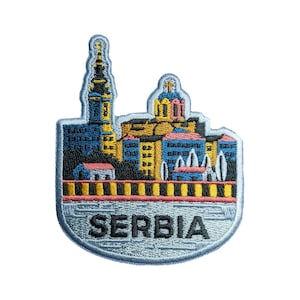 May include: Embroidered patch depicting a cityscape with a church and buildings in blue, yellow, and pink colours. The patch has a grey background and the word "SERBIA" in black lettering.