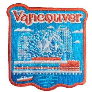 May include: Embroidered patch with the word "Vancouver" in orange. The design shows a blue and white cityscape, including a geodesic dome, two skyscrapers, and a boat, set against a blue background with orange trim.