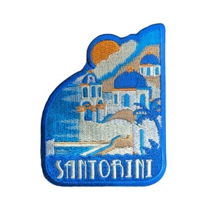 Peut inclure: Patch brodé bleu et blanc représentant un bâtiment blanc avec des accents bleus et un palmier. Le texte "Santorini" est brodé en blanc sur un fond bleu.