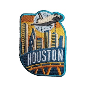 May include: Embroidered patch with a blue, yellow, and orange cityscape of Houston, Texas. A space shuttle flies over the city with the word "HOUSTON" in white text.