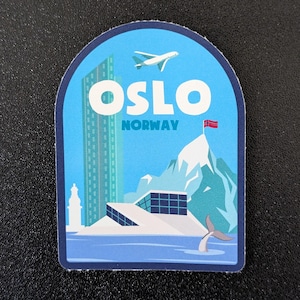 May include: A blue and white sticker with a graphic of a city skyline, a plane, a mountain, and a whale tail. The sticker says "Oslo, Norway".