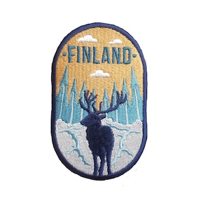 Peut inclure: Un patch brodé représentant un renne bleu debout dans une forêt enneigée. Le patch est de forme ovale et a un fond jaune avec le mot "FINLAND" en lettres bleues.
