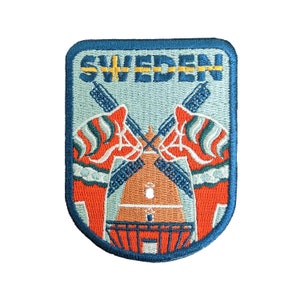 May include: A blue embroidered patch with the word "SWEDEN" in yellow letters. The patch features two red and white Dala horses facing each other, a yellow and blue Swedish flag, and a small orange building with a white roof.